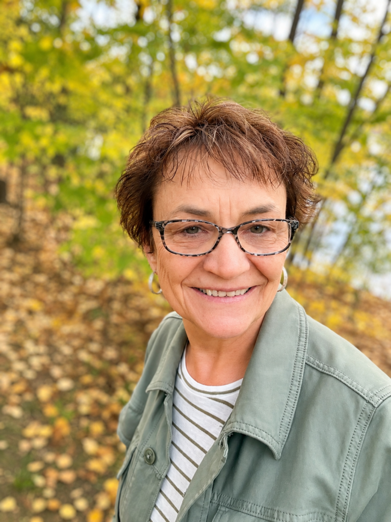 Kathy Ann smiling outdoors in a fall forest.